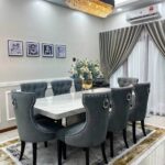 Transform your dining space with the luxurious Godwin Series IX Premium 8 Seater Dining Set. This elegant dining table features a stunning marble top, paired with plush gray tufted chairs for ultimate comfort and style. Perfect for modern homes, this sophisticated set is beautifully complemented by a statement chandelier, stylish curtains, cherished family photos, and a vibrant floral centerpiece—creating a warm and inviting atmosphere ideal for gatherings and celebrations. Upgrade your home décor today with the Godwin Series IX marble dining set for 8 and experience the perfect blend of luxury and functionality in your modern dining room.